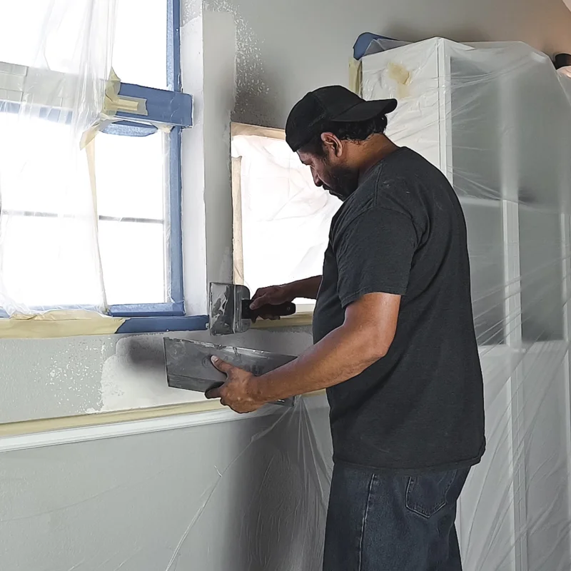 Roland doing drywall work - applying compound near a window